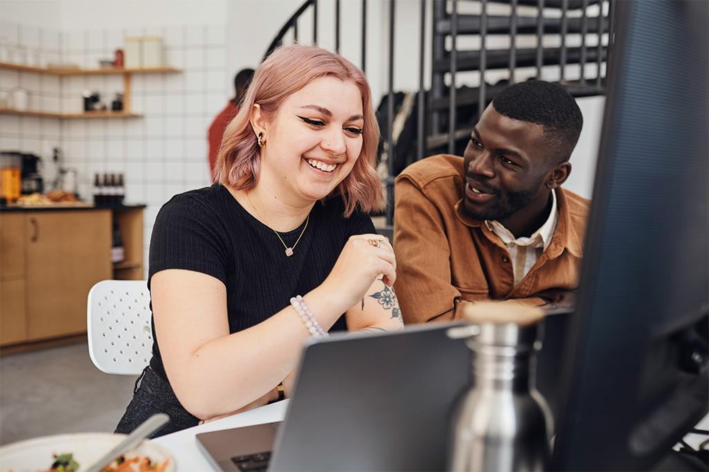 two people sitting at work desk smiling